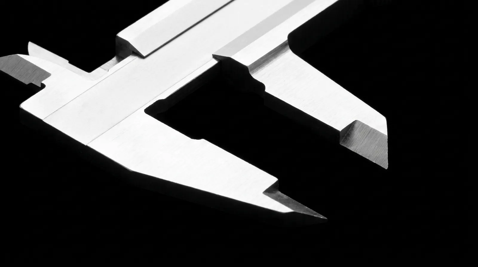 Un pied à coulisse métallique de précision, mâchoires ouvertes, posé sur fond noir et éclairé de manière à faire ressortir l’arête de ses becs.